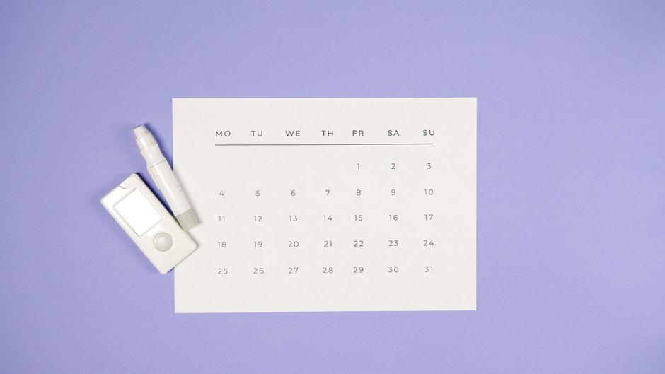 Minimalist setup of a glucometer, lancet pen, and calendar on a light purple background.