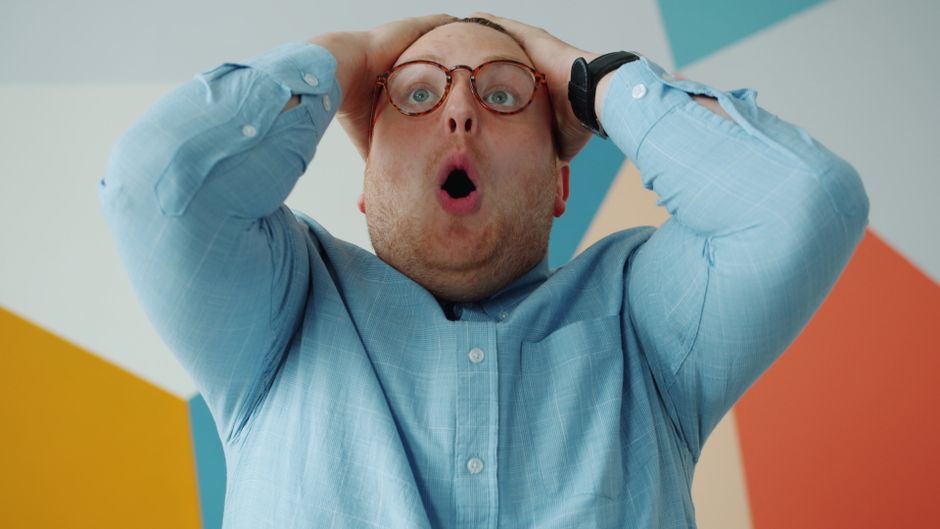 A man with round glasses expresses surprise holding his head in disbelief.
