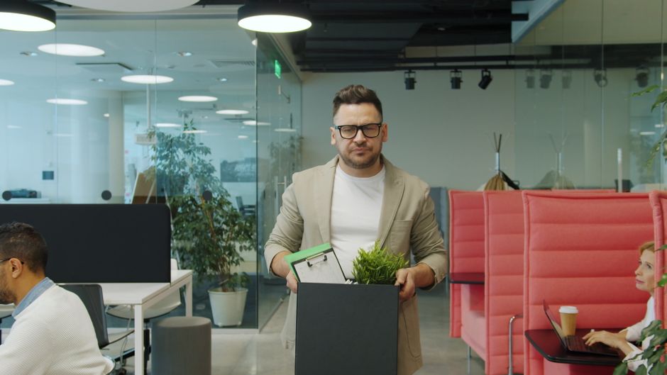 Man carrying a box of belongings, exiting office after job termination.